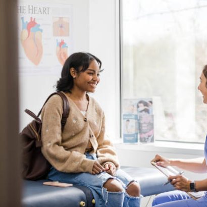 The young adult female patient smiles while listening to the nurse give an encouraging update regarding her medical exam that was recently completed.